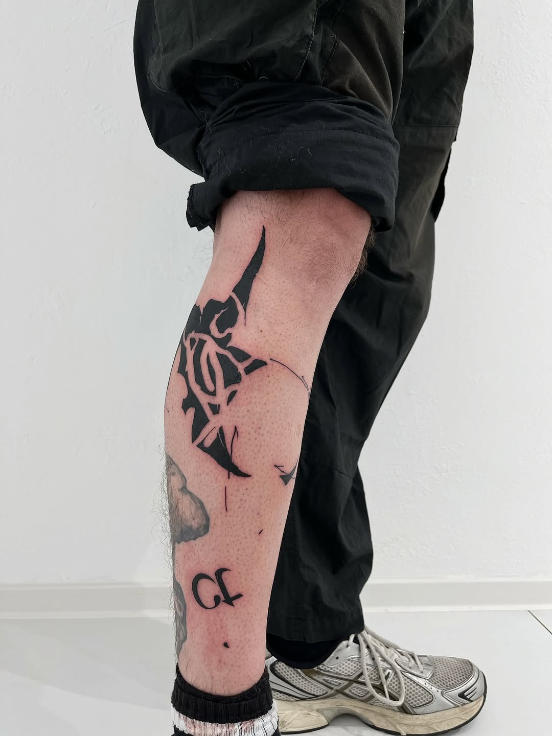 Bold black geometric tattoo by Andrii Volkov with angular tribal-inspired forms and dotwork patterns on leg, showcasing street art documentation style