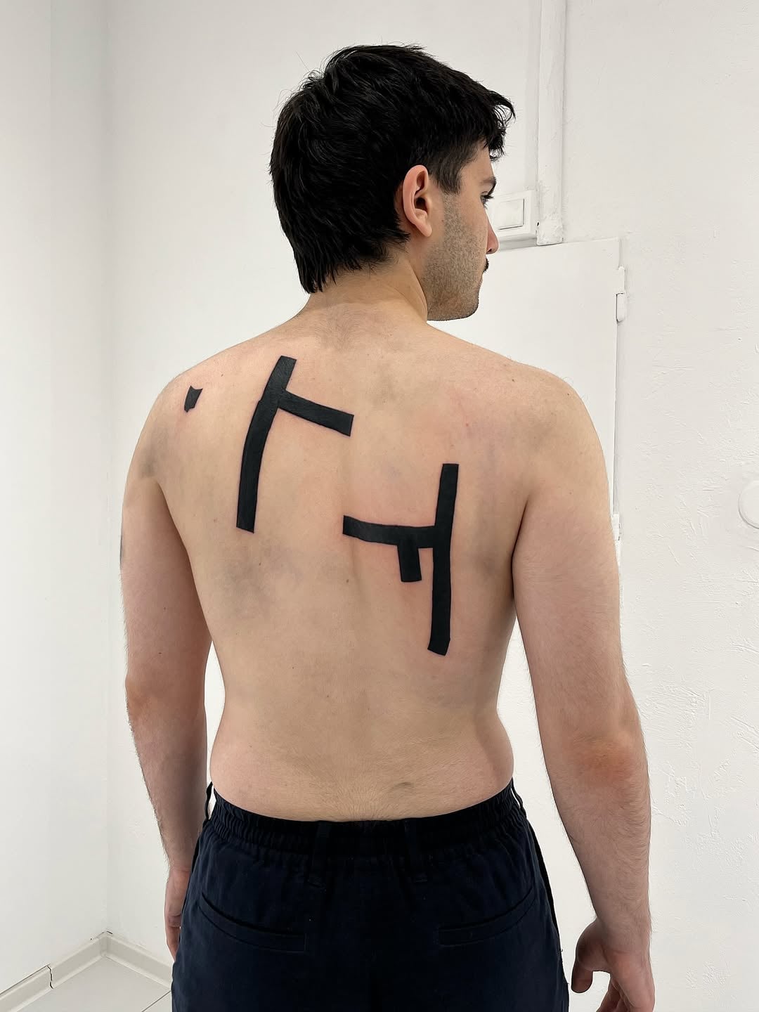 Minimalist architectural tattoo by Andrii Volkov featuring bold black geometric lines forming abstract structural shapes across the back